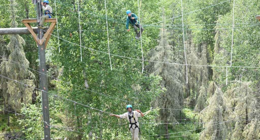 two students are suspended by ropes as they make their way through a ropes course on an outward bound course